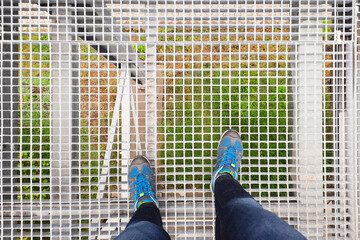 Close up of female legs in blue sneakers standing on Steel grating stairs. Feet in sports shoes....