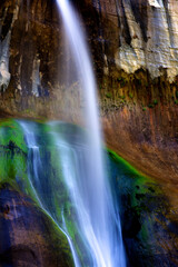 Majestic, narrow waterfall over stone cliff near colorful cave