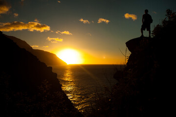 Silhouette of man standing on Hawaiian cliff and staring out at sunset over ocean