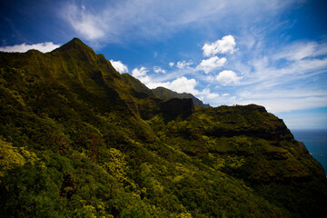 Side of beautiful, lush Hawaiian mountain and scattered clouds above