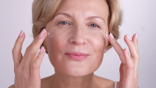 Empowered woman in her 50s engages in her evening selfcare routine, gently applying night cream on her face. Anti-aging beauty rituals.