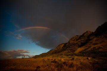 Glowing rainbow over rocky mountains at dusk - low shot