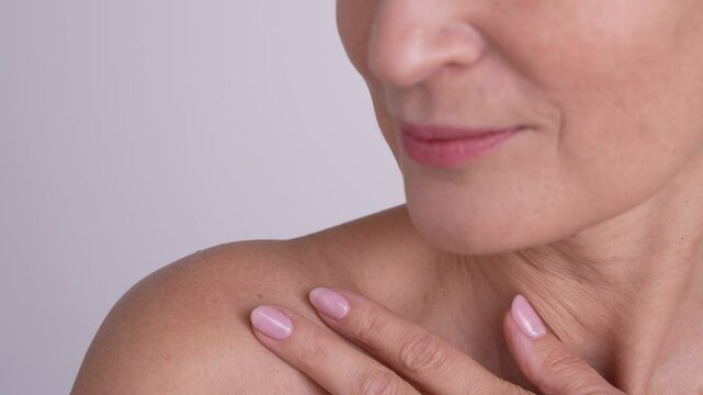 Close-up portrait of a natural mature female gently touching her shoulder and neck. Beauty anti-aging routine, self-care, facial skincare.