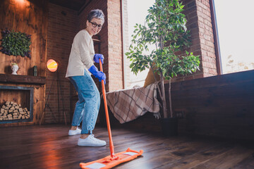 Charming elderly woman enjoying a leisurely weekend at home, cleaning her modern apartment with joy and enthusiasm