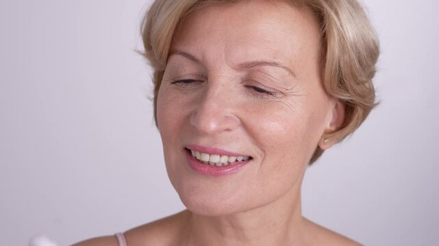 Naturally beautiful aging woman on her skincare journey using face massage tool. Positive graceful aging and anti-aging beauty routine