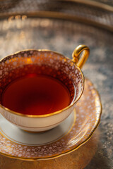 a gold and pink pattern teacup and saucer set with black tea on a silver tray