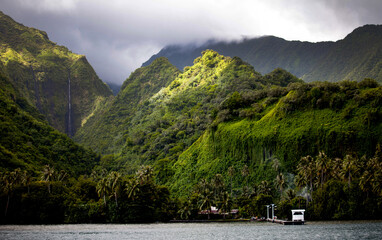 Tall, lush Hawaiian mountains near dock and ocean water. Storm clouds above