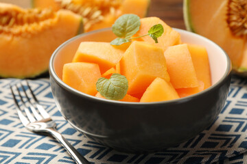 Pieces of ripe Cantaloupe melon in bowl and fork on table, closeup