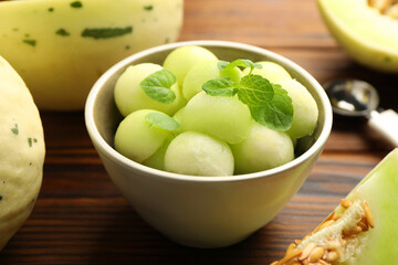 Melon balls in bowl and fresh fruit on wooden table, closeup
