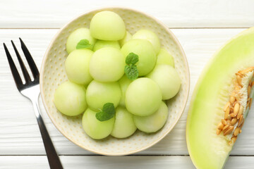 Melon balls in bowl and fresh fruit on wooden table, top view