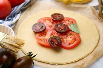 Raw galette with tomato and basil on white tiled table, closeup