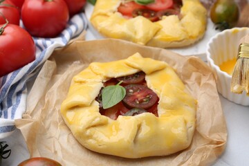 Raw galettes with tomato and basil on white tiled table, closeup