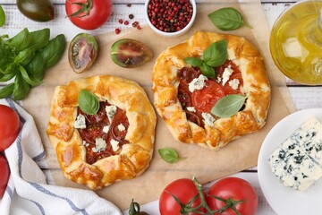 Tasty galettes with tomato, basil and cheese on white wooden table, flat lay