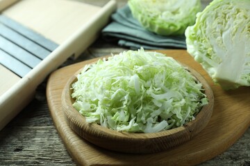 Fresh shredded cabbage and shredder on wooden table, closeup