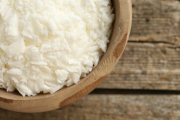 White soy wax flakes in bowl on wooden table, closeup