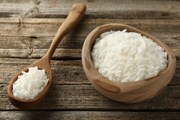 White soy wax flakes in bowl and spoon on wooden table, closeup