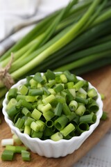 Chopped green onion in bowl and stems on table, closeup