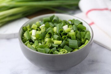Chopped green onion in bowl on white table, closeup
