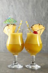 Tasty pineapple cocktail in glasses served on grey table