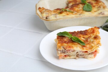 Piece of delicious cooked lasagna with basil on white tiled table, closeup. Space for text