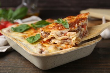 Taking piece of delicious cooked lasagna with basil at wooden table, closeup