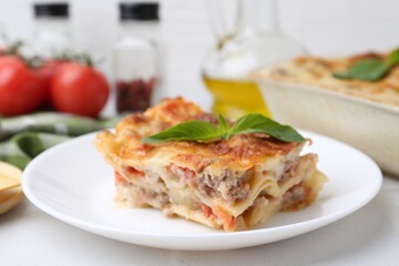 Piece of delicious cooked lasagna with basil on white table, closeup
