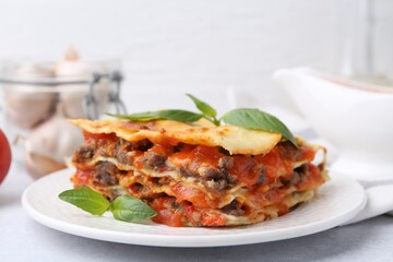 Delicious cooked lasagna with basil on light table, closeup