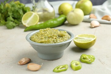 Delicious salsa sauce in bowl and products on light textured table, closeup