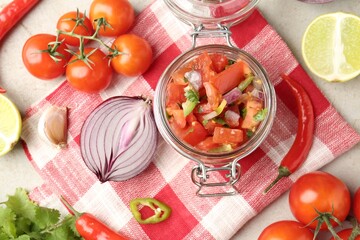 Delicious salsa (Pico de gallo) in jar and ingredients on light textured table, flat lay