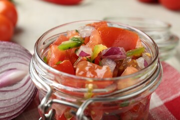 Delicious salsa (Pico de gallo) in jar and onion bulb on table, closeup