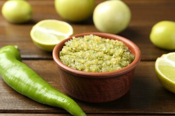 Delicious salsa sauce in bowl and products on wooden table, closeup