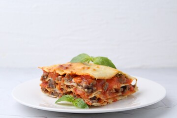 Piece of delicious cooked lasagna with basil on white table, closeup