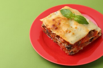 Piece of delicious cooked lasagna with basil on green background, closeup. Space for text