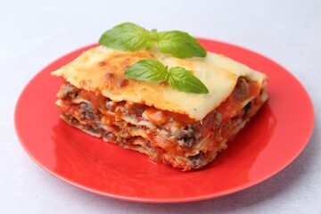 Piece of delicious cooked lasagna with basil on light table, closeup