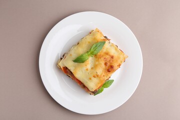 Piece of delicious cooked lasagna with basil on beige background, top view