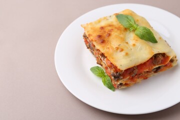 Piece of delicious cooked lasagna with basil on beige background, closeup. Space for text