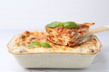 Delicious cooked lasagna with basil in baking dish on white textured table, closeup
