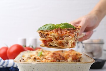 Woman taking piece of delicious cooked lasagna with basil at table, closeup