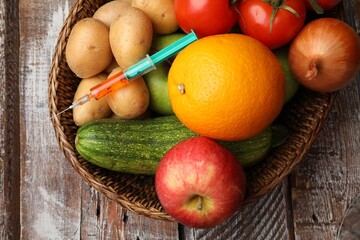 GMO concept. Different products and syringe in basket on wooden table, top view