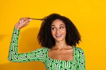 Charming young woman with curly hair in a vibrant green top against a yellow background, expressing joy and happiness.