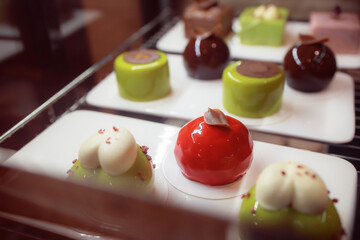 Delicious soft desserts on display. A variety of chocolate cakes in the refrigerator. Close-up view of a delicious Asian cake. Signature ice cream on disposable tableware. Green, red and brown cakes.