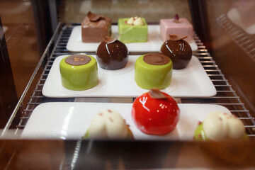 Delicious soft desserts on display. A variety of chocolate cakes in the refrigerator. Close-up view of a delicious Asian cake. Signature ice cream on disposable tableware. Green, red and brown cakes.