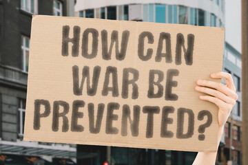 The phrase 'How can war be prevented?' on a banner in a person's hand. Human holds a cardboard with...