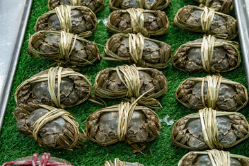 Many hairy crabs(Raw shanghai hairy crabs) wrapped in bamboo shoots, displayed on a green carpet at a market counter.