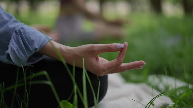 A close-up of a woman hand with light lavender nail polish in a meditative gesture, resting gracefully on her knee during yoga in a tranquil park. The elegant manicure adds a touch of refinement
