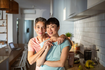Lesbian couple smiling portrait in kitchen with healthy breakfast and smoothie
