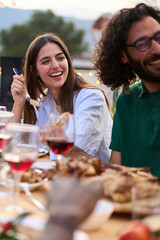 Vertical. Young adult Caucasian couple smiling sitting at table at friendly summer barbeque outdoors. Joyful millennial people enjoying laughing reunion BBQ food in weekend event eating rooftop 