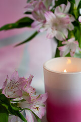 A glowing candle with Peruvian lilies in a vase as a backdrop.