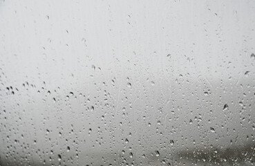 Droplet on the windows, close up. Raindrops on glass with grey clouds in background. Rainy day. Water drops. Rain is falling.