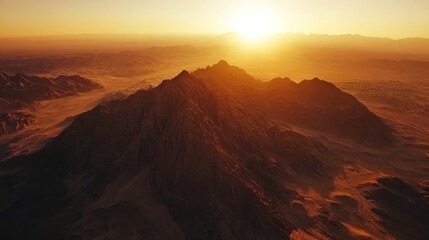 An aerial view of a mountain range at sunset, with the sun shining brightly in the distance.